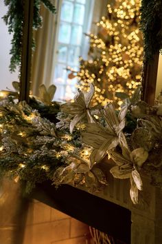 a christmas tree is lit up in front of a fireplace with garland and lights on it