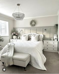 a white bed sitting under a chandelier in a bedroom next to a window