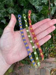 a hand holding three different colored bracelets on it's palm with leaves in the background