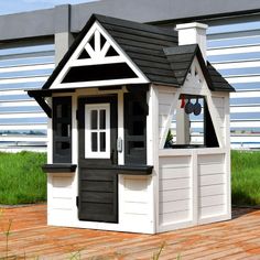 a small white and black dollhouse on a wooden floor next to a fenced in area