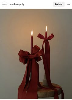 two candles are on top of a table with red ribbons and bows around the candle holders