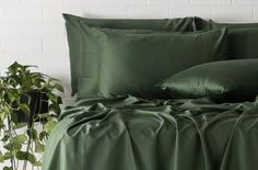 a bed with green sheets and pillows next to a potted plant