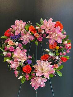 an arrangement of flowers arranged in a heart - shaped wreath on top of a stand