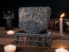 candles are lit next to an ornate box on a table with other items in the background