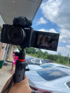 a person holding up a video camera in front of a building with cars parked on the street