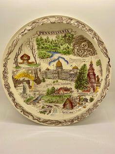 a decorative plate with the map of pennsylvania painted on it's sides and features buildings, trees, and mountains