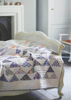 a bed with a quilt on it in front of a fireplace