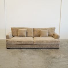 a tan couch sitting in front of a white wall with four pillows on top of it