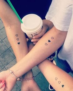 two girls with matching tattoos on their arms holding a coffee cup and a green straw