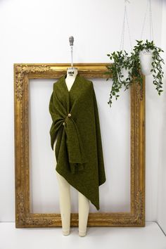 a green shawl draped over a mannequin in front of a gold frame