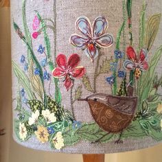 a lamp shade decorated with flowers and birds on it's side, sitting on a wooden table