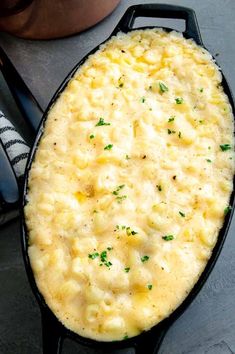 an oval casserole dish with cheese and parsley on top, next to a spoon