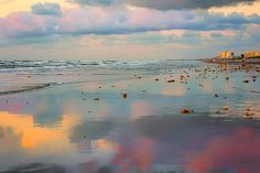 the sky is reflected in the wet sand on the beach as clouds loom overhead