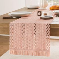 a pink table runner with tassels and plates on the table in front of a window