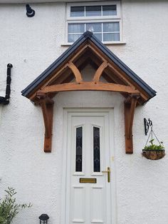 a white house with a wooden front door and window above the entrance to it is decorated with potted plants