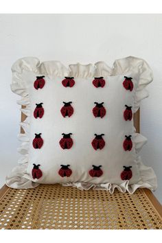 a white pillow with red ladybugs on it sitting on a wicker chair