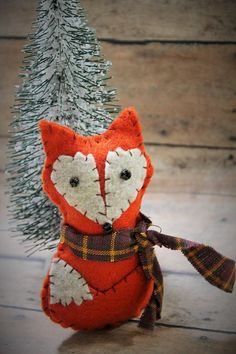 an orange and white stuffed animal next to a small christmas tree on a wooden floor