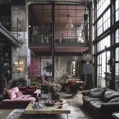 a living room filled with lots of furniture next to tall windows on top of a wooden floor