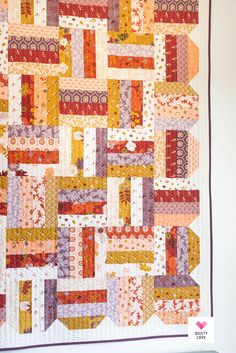 an orange and yellow quilt hanging on the wall in front of a white wall with purple trim