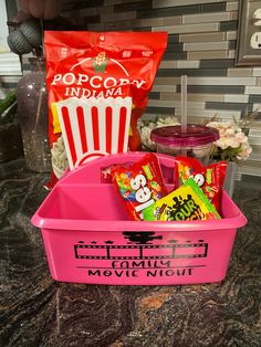 a pink plastic container filled with candy and snacks sitting on top of a counter next to a bag of popcorn