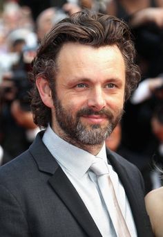 a man in a suit and tie posing for the camera with people behind him taking pictures