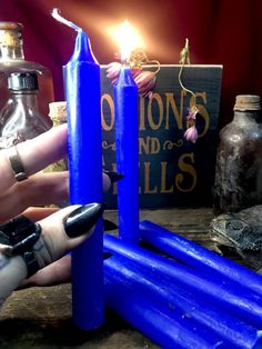 a person holding a blue candle in front of some bottles and other items on a table