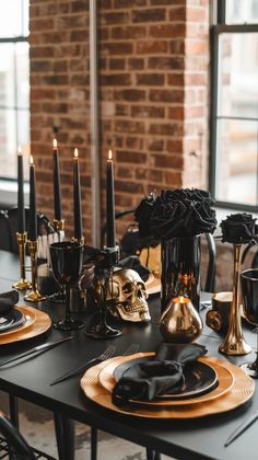 a dining table with black and gold plates, candles and skulls on the plate holders