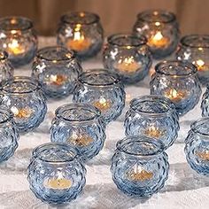 many clear glass candles are lined up on a white tablecloth with gold dots in them