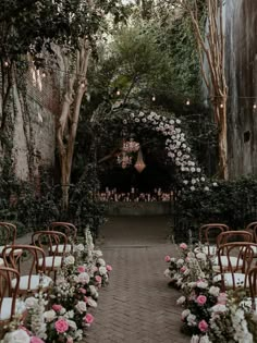 an outdoor ceremony set up with white and pink flowers on the aisle, surrounded by greenery