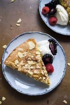 two plates topped with pie and berries on top of a wooden table next to each other