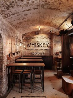 the inside of a brick building with tables and stools in front of an old sign