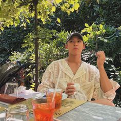 a young man sitting at an outdoor table eating food and drinking from a straw in his hand