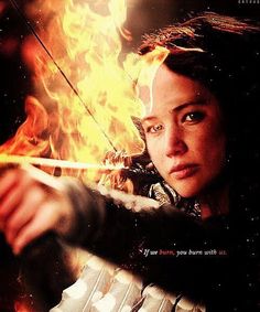 a woman holding a bow and arrow in front of fire