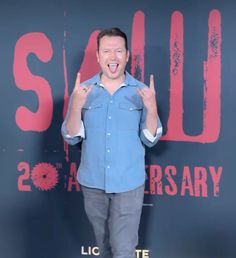 a man standing in front of a red and black background giving the peace sign with his hands