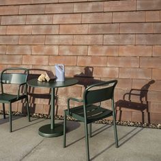 two green chairs and a table against a brick wall