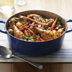 a blue pot filled with meat and vegetables on top of a table next to a glass of wine