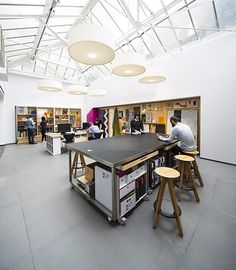 people are sitting at tables in an open area with bookshelves and desks