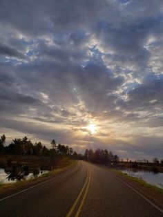 the sun is setting on an empty road near some water and trees in the distance