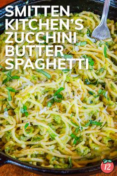 a skillet filled with spaghetti and broccoli on top of a wooden table