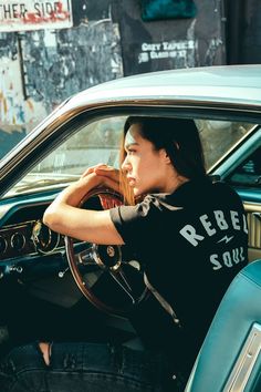 a woman sitting in the driver's seat of a car with her hand on the steering wheel