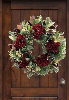 a wreath with red flowers and greenery hangs on the front door to welcome guests