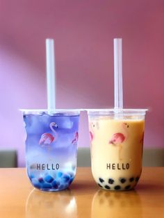 two drinks sitting next to each other on top of a wooden table in front of a pink wall