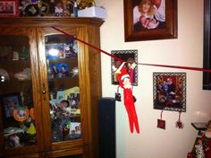 an elf hanging on a red string in the corner of a room next to a china cabinet