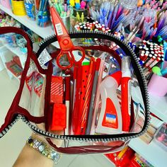 a person holding a bag full of school supplies in it's hand, with scissors and pencils on the table