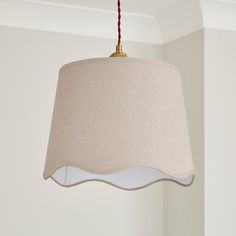 a beige lamp hanging from a ceiling with a red cord attached to the light fixture