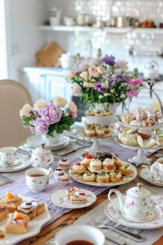 a table topped with lots of plates and cups filled with pastries next to flowers