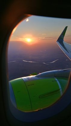 an airplane wing with the sun setting in the sky as seen through it's window