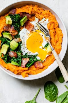 a bowl filled with mashed sweet potatoes topped with bacon, avocado and an egg