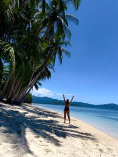 a woman standing on top of a sandy beach next to palm tree's and ocean