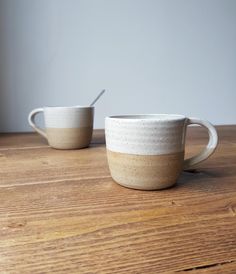 two white and brown cups sitting on top of a wooden table next to each other